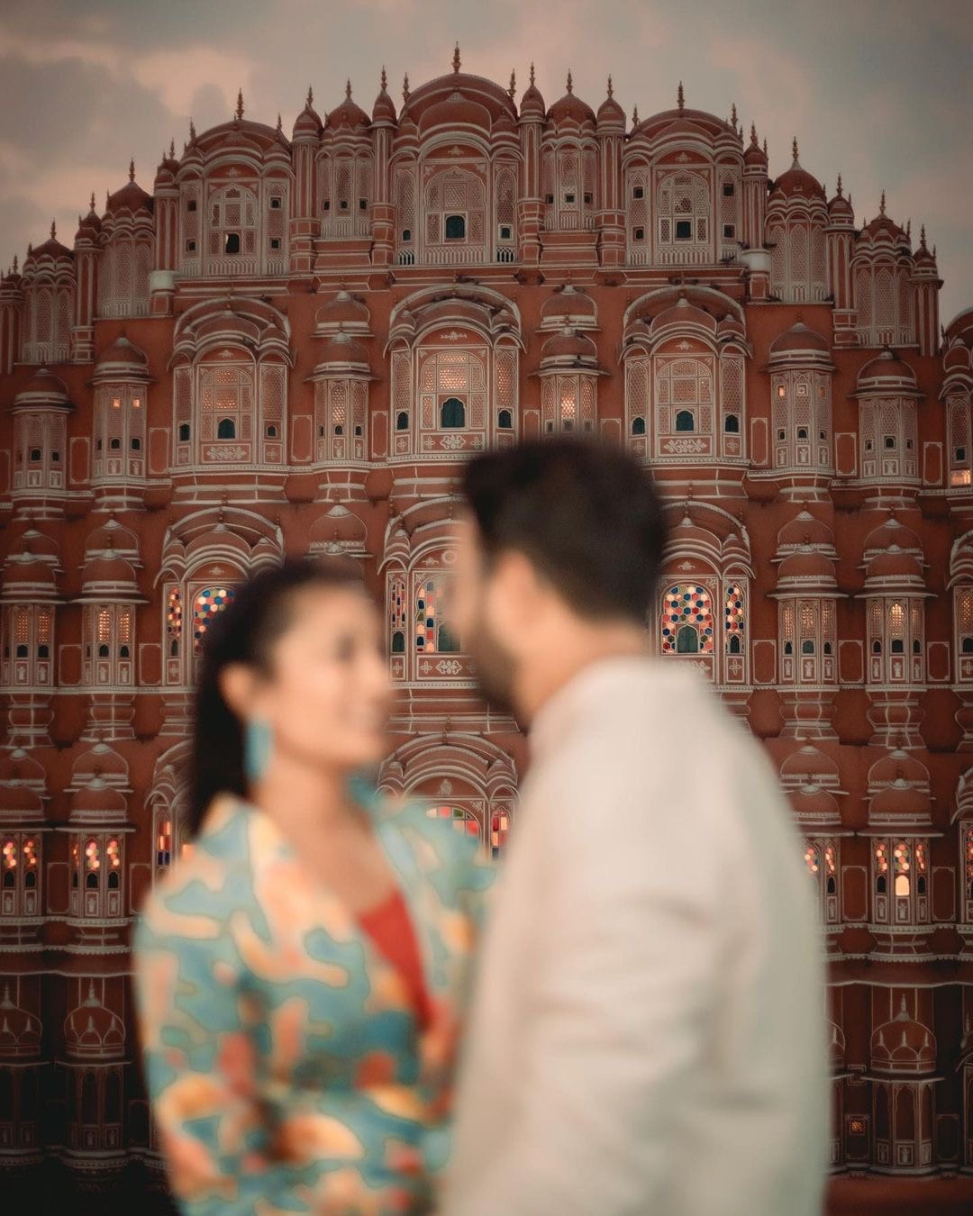 The stained glass windows of Hawa Mahal in focus, the couple soft in the foreground