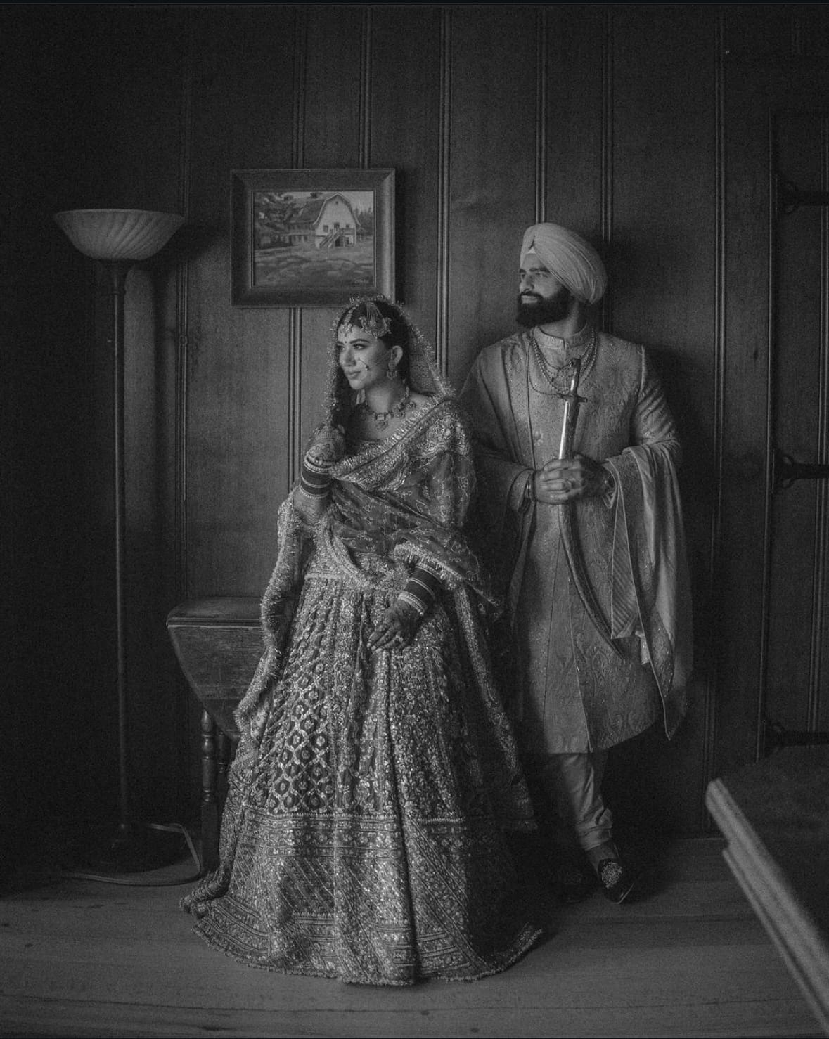 Bride and groom in a panelled room in black and white, he holds a kirpan at his side