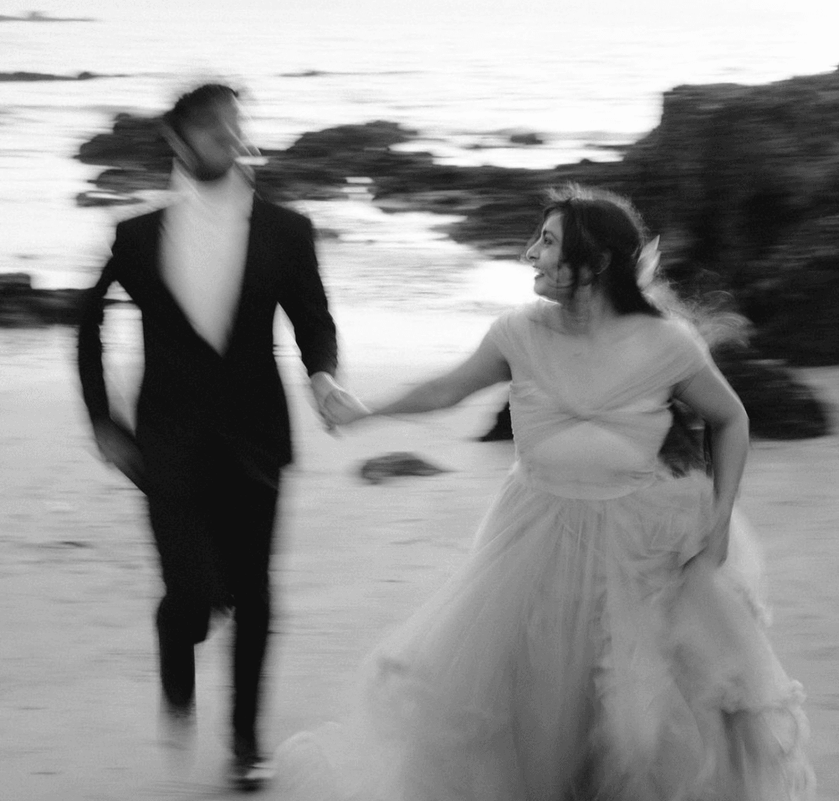 Motion blurred frame of the couple running hand in hand along a beach at first light