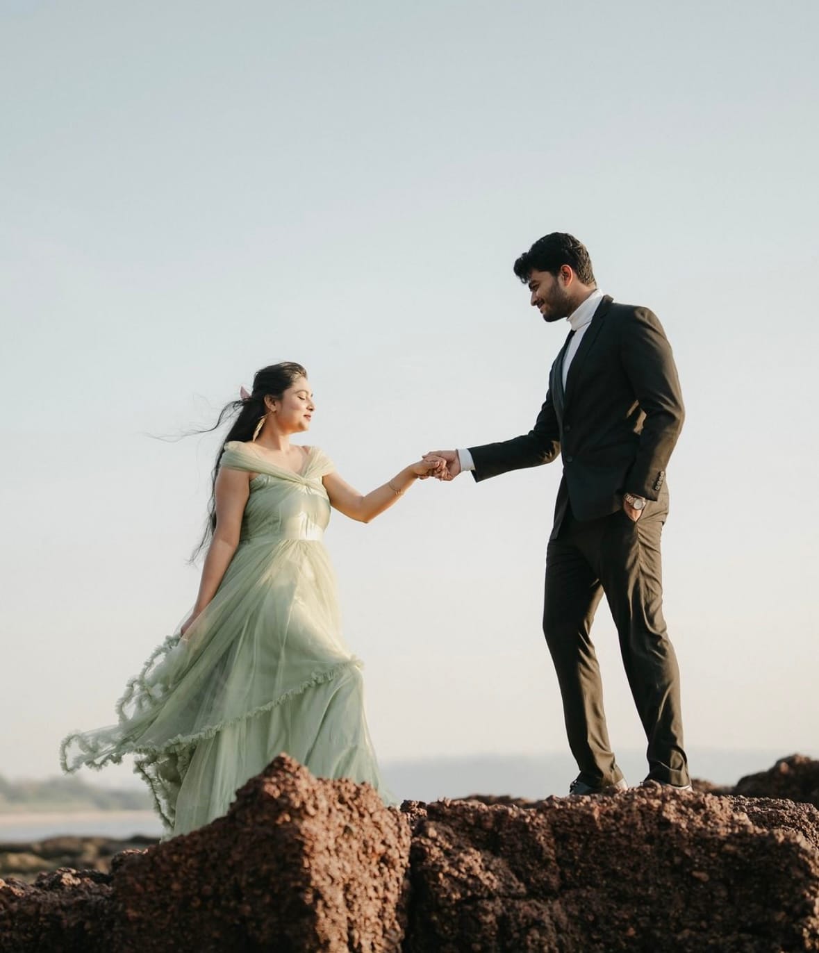 He pulls her up onto a rock by the sea, her mint tulle dress lifting in the wind