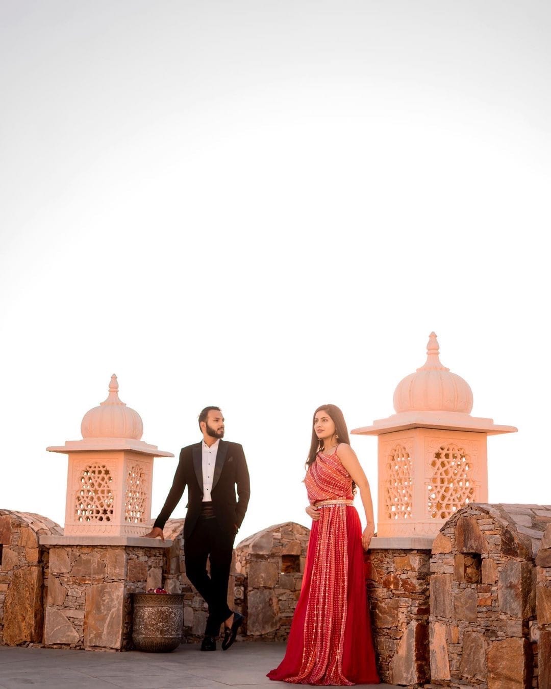 Couple on a fort rampart between two carved chhatris under a bleached morning sky