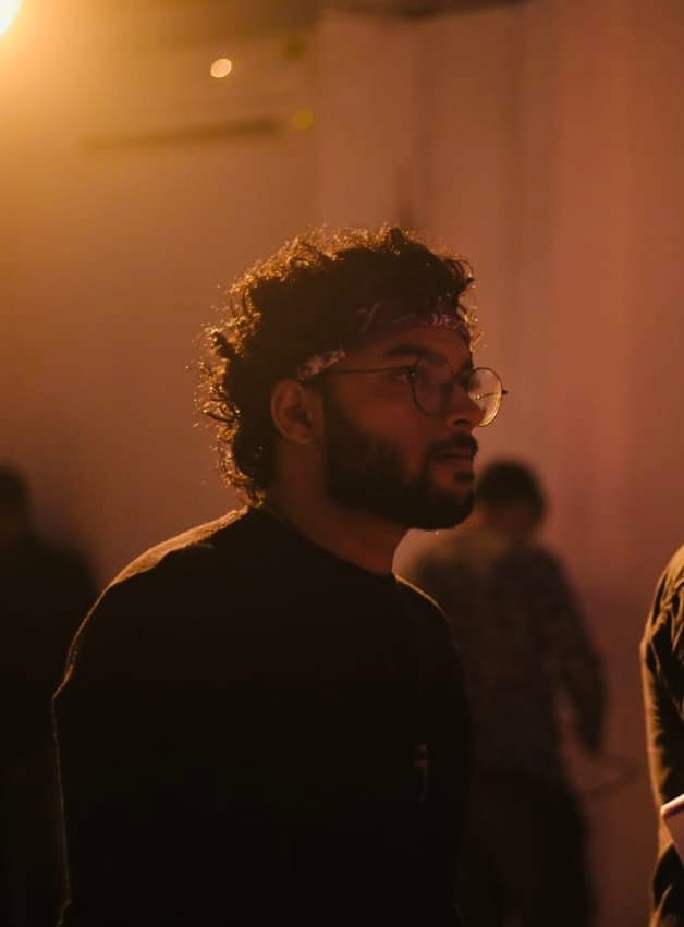 Naman Gupta on set, lit by an amber practical light, looking off camera