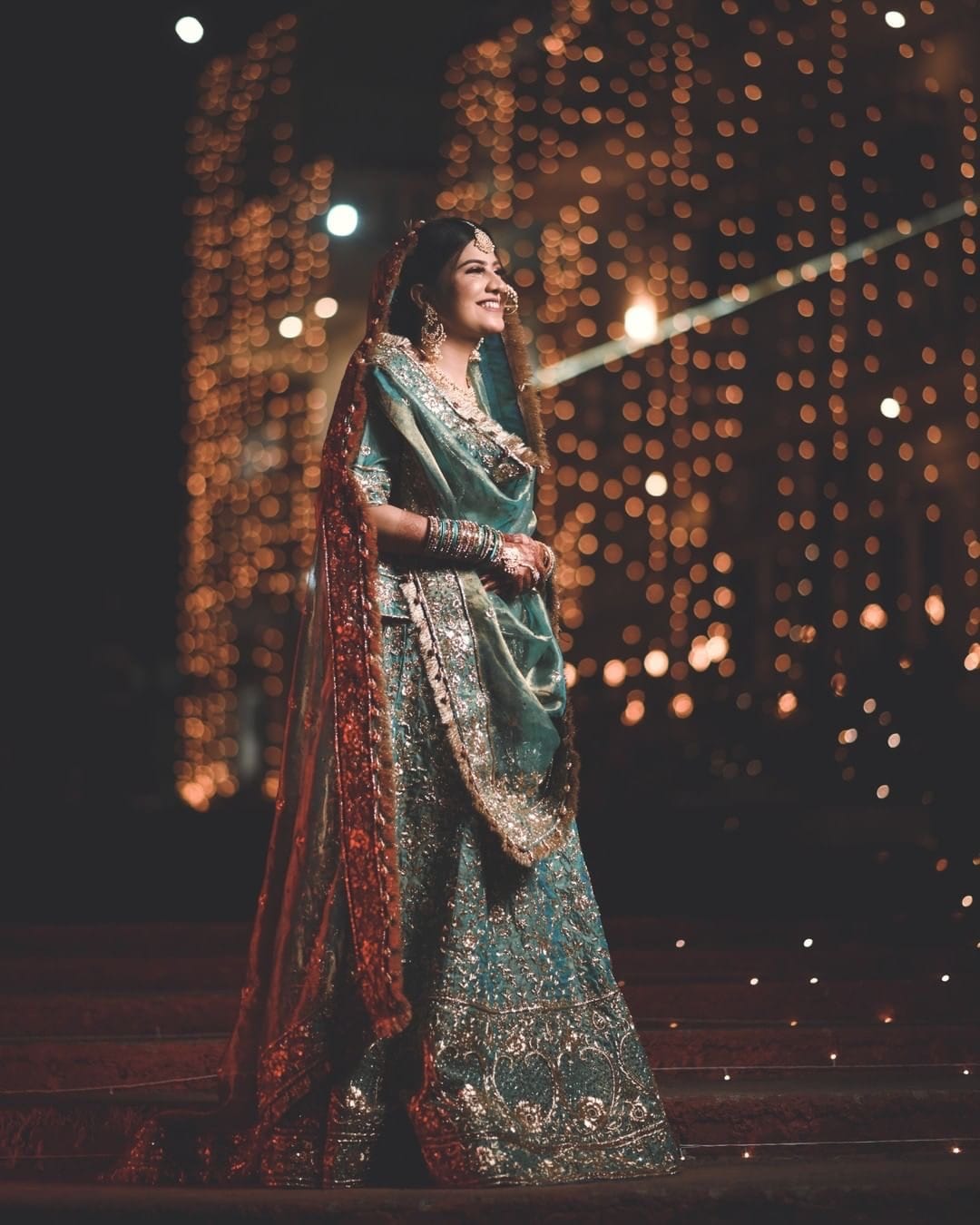 Bride in a teal and gold lehenga against a curtain of warm fairy lights