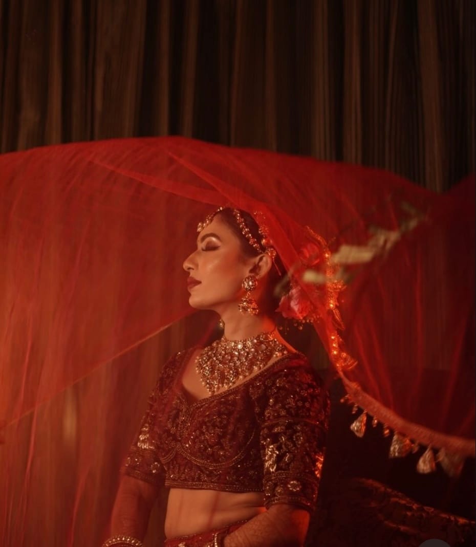 A red net veil lifting away from the bride against a dark curtain