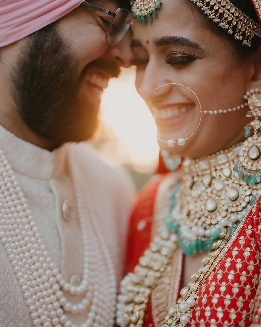 Bride and groom laughing forehead to forehead in golden hour light, her nath and his pearl strands catching the sun