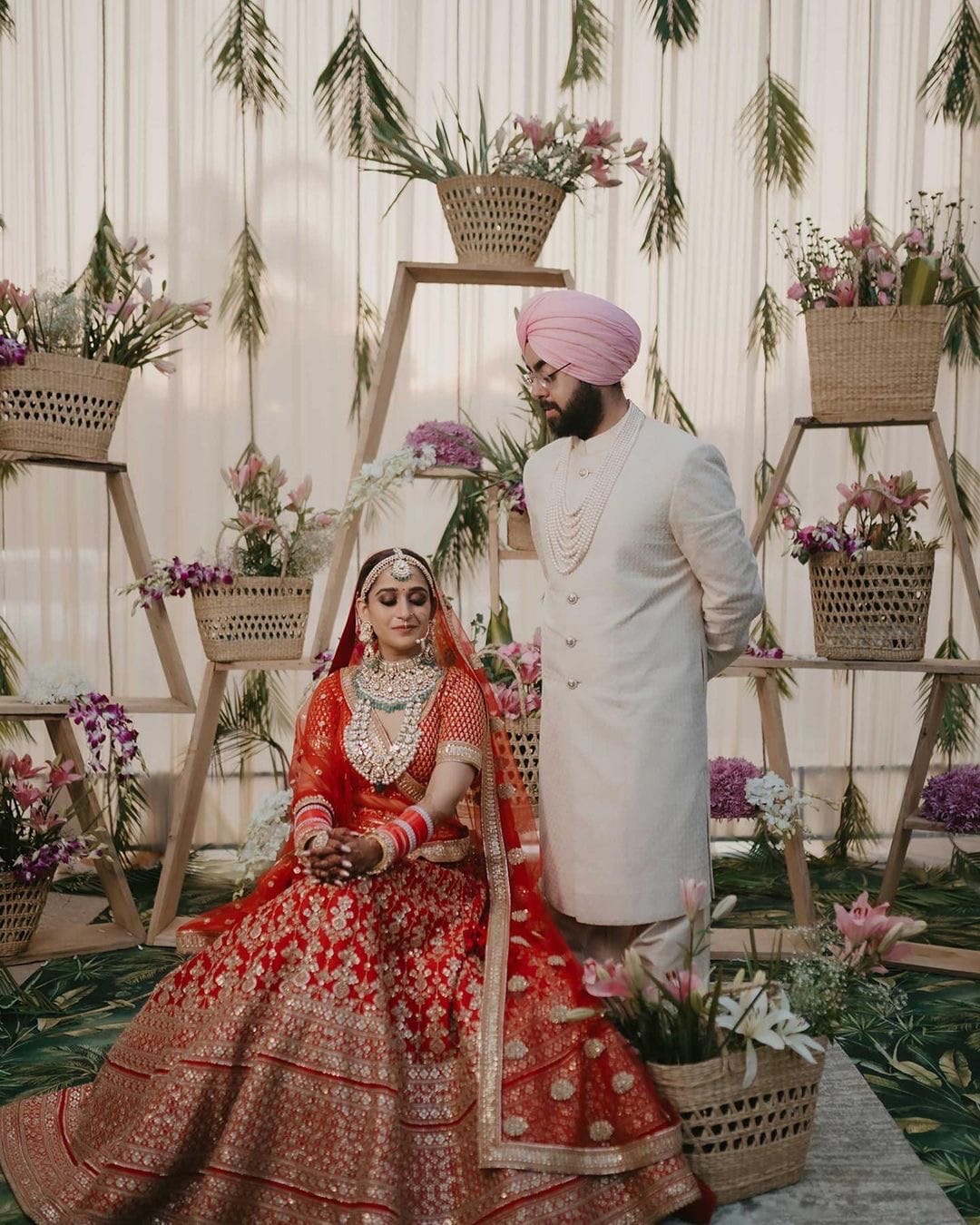 Bride seated in front of a cane and lily backdrop, the groom standing beside her in ivory